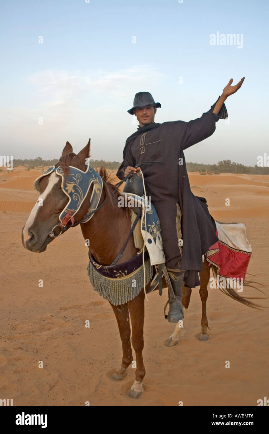 Un tour guida vestita come Zorro si trova sul suo cavallo con le braccia aperte nel deserto del Sahara nei pressi dell'oasi Ksar Ghilane, Tunisia Foto Stock