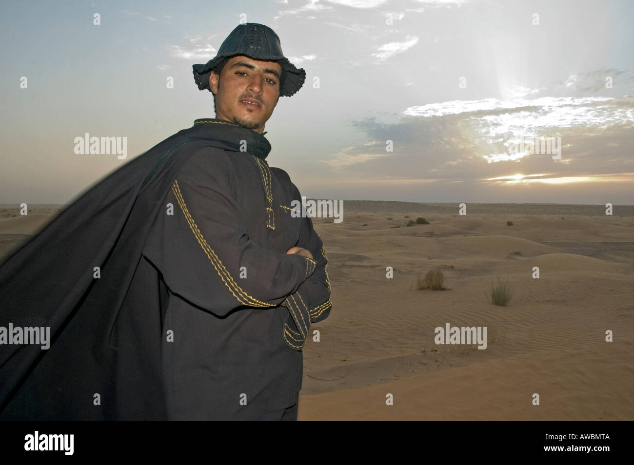 Un tour guida vestita come una Zorro pone di fronte al tramonto nel deserto del Sahara nei pressi dell'oasi di Ksar Ghilane, Tunisia. Foto Stock