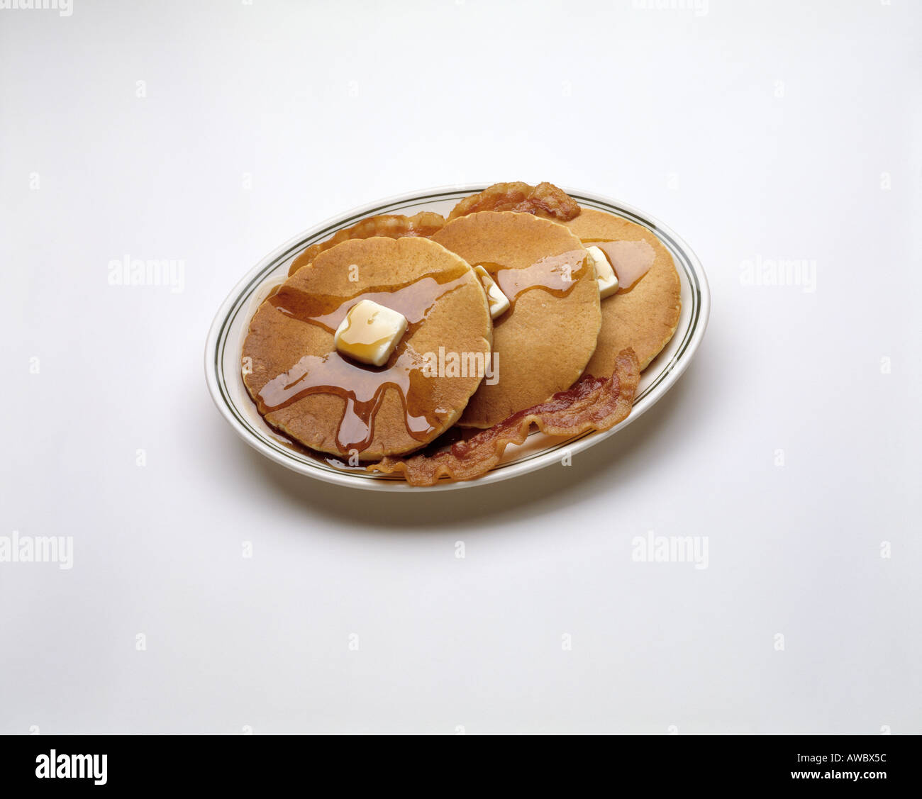 Pila di piastre di 3 tre frittelle di burro fuso sciroppo di due 3 inclinate di bacon fast food sostanziosa colazione sfondo bianco Foto Stock