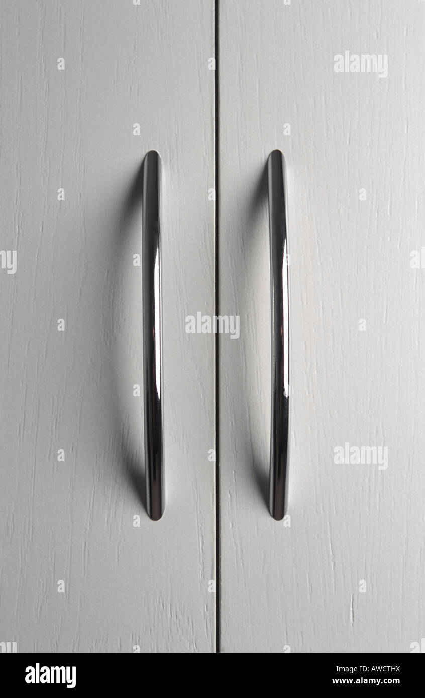 Coppia di maniglie delle porte cromate su bianco antine Foto Stock