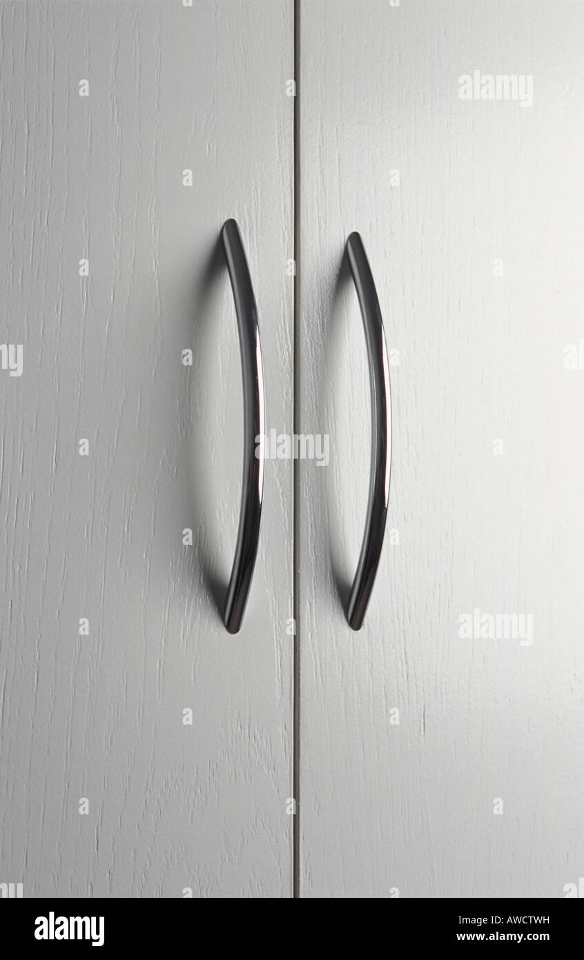 Coppia di maniglie delle porte cromate su bianco antine Foto Stock
