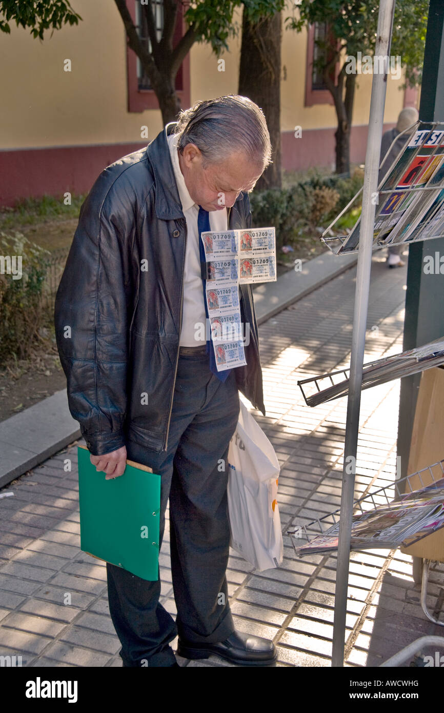 Con i biglietti della lotteria che egli vende agganciata al suo cappotto di un venditore di strada si prende una pausa per leggere un giornale display in Siviglia Spa Foto Stock
