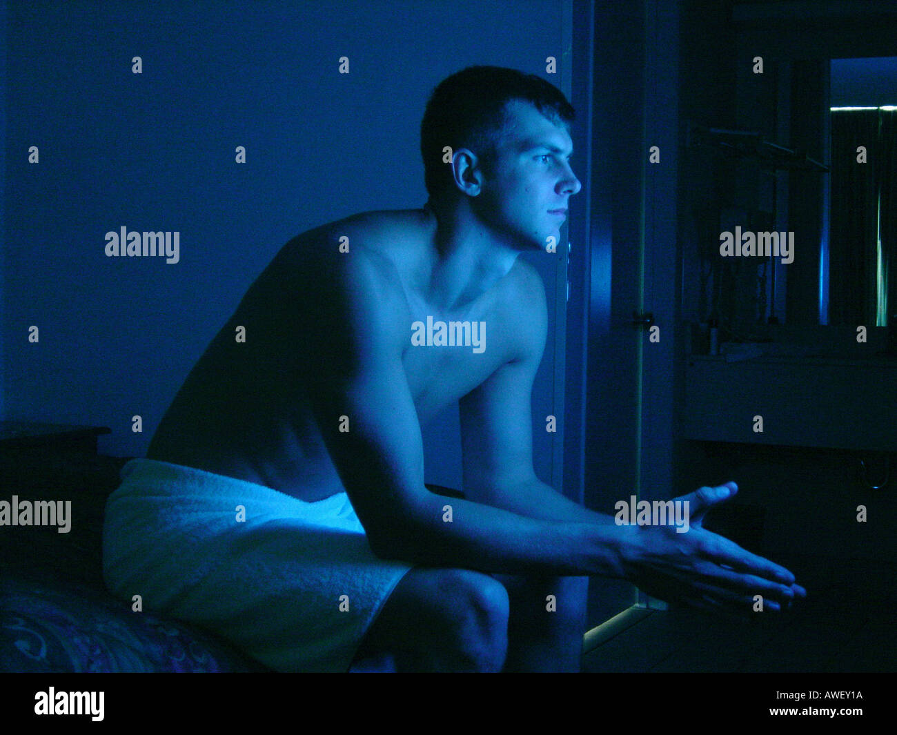 Ritratto di parzialmente uomo nudo illuminato da una televisione che egli è  seduto su un letto di guardare la TV Foto stock - Alamy