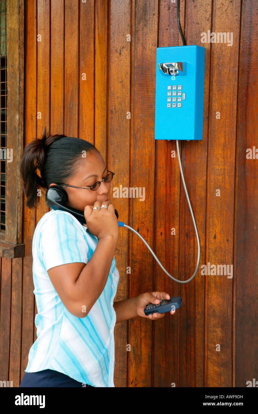 Giovane donna su un telefono pubblico con un telefono cellulare in mano, amerindi, tribù degli arawak, Santa Missione, Guyana, Sud un Foto Stock