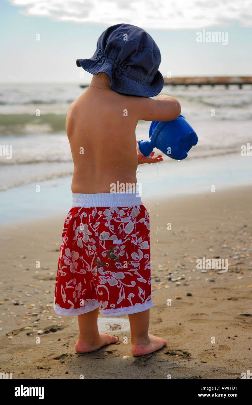 Ragazzino sulla spiaggia a giocare con un annaffiatoio, Caorle, Veneto, Italia Foto Stock