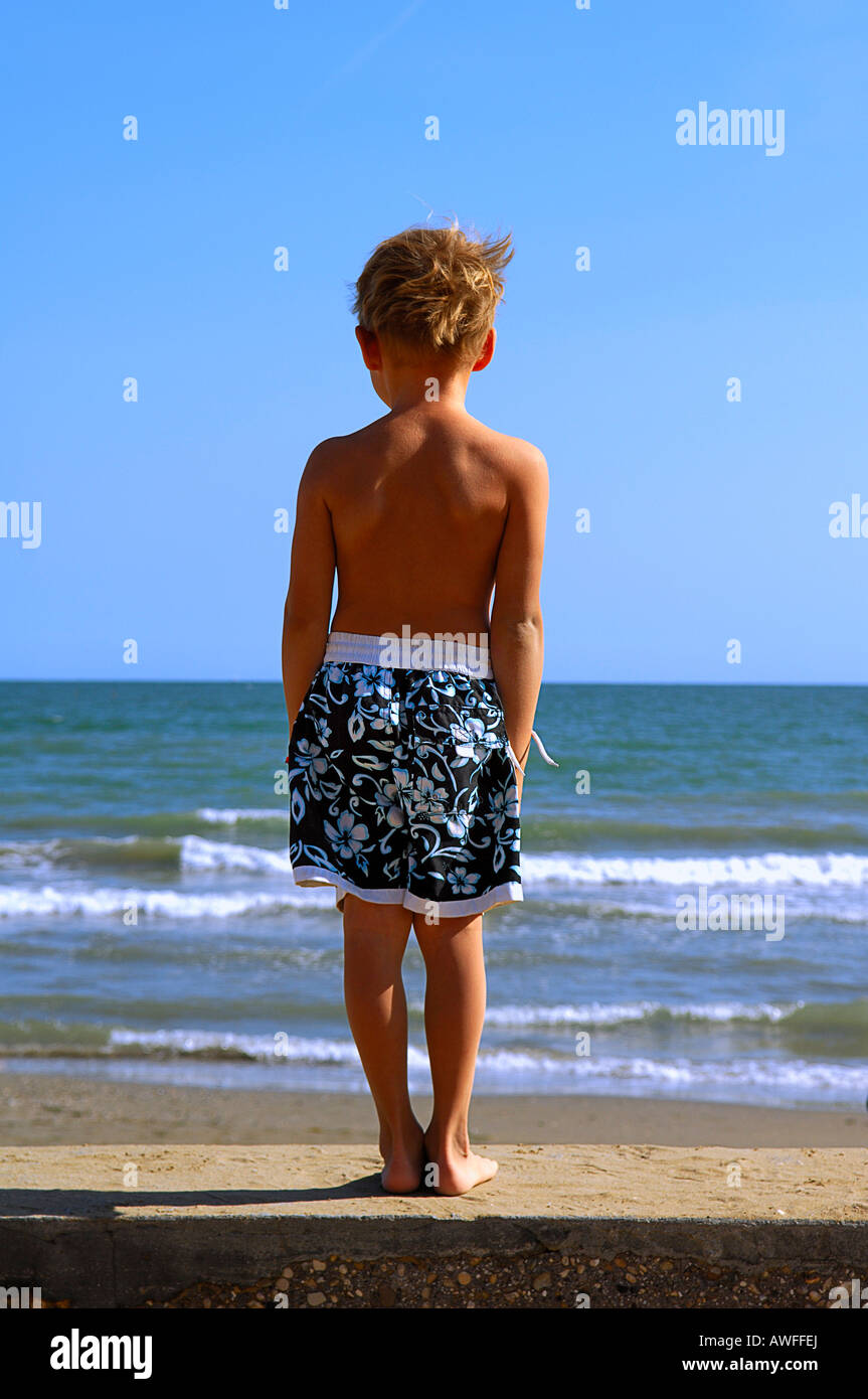 Ragazzo sulla spiaggia guardando fuori del mare, Caorle, Veneto, Italia Foto Stock