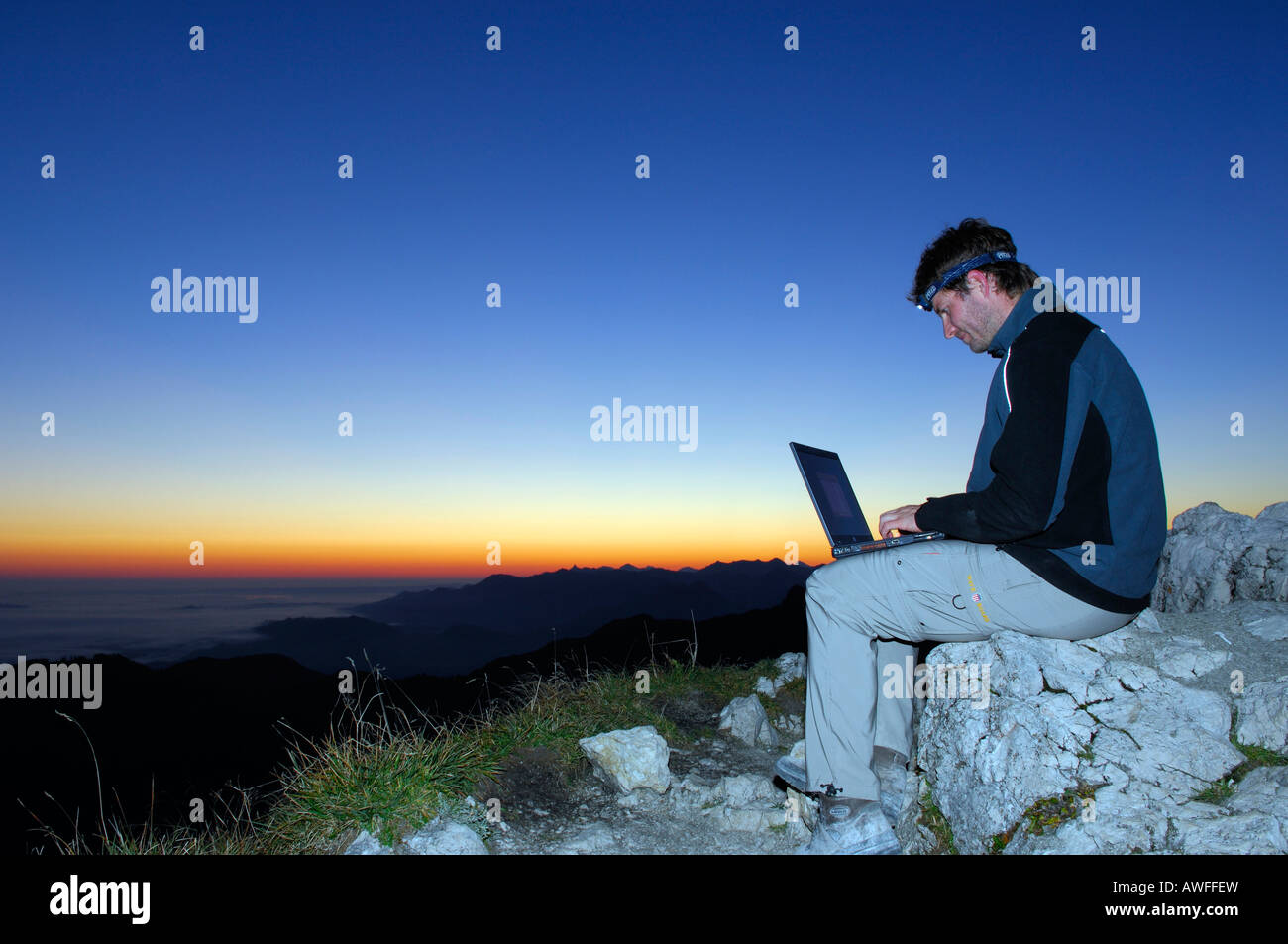 Uomo con notebook a sunrise in cima a una montagna, Breitenstein Mountain, prealpi bavaresi, Wendelstein Gruppo, Alta Baviera, Bava Foto Stock