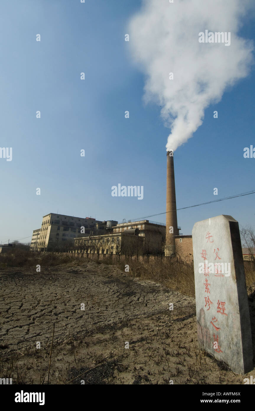 Cavalletto di lapidi in un cimitero accanto a un fumo eruttazioni fabbrica a ovest di Pechino Foto Stock