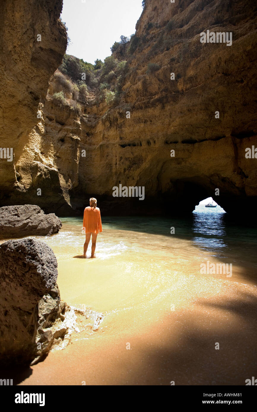 Una donna cammina su una spiaggia all'interno di una grotta lungo il Portogallo Algarve costa. Foto Stock