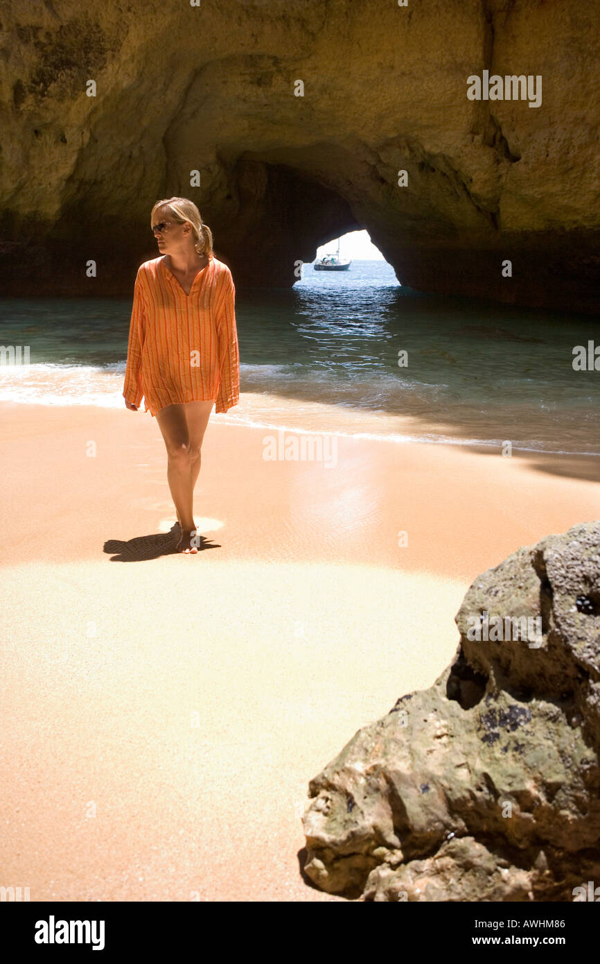 Una donna cammina su una spiaggia all'interno di una grotta lungo il Portogallo Algarve costa. Foto Stock