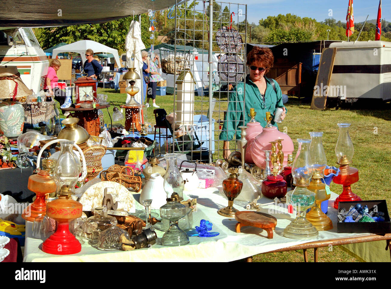 Donna esamina gli elementi sul tavolo al mercato delle pulci Swap Meet vendita compresi numero di molto vecchie lampade a olio economia Foto Stock