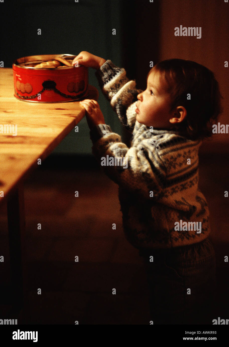 Il Toddler raggiungendo per i cookie sul tavolo, vista laterale Foto Stock