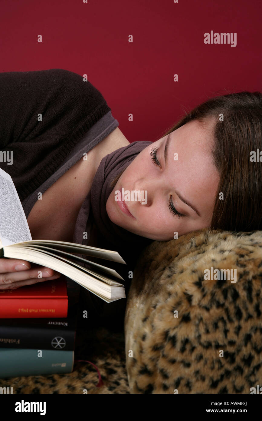 Ritratto di una ragazza, pre-teen, early teens posa su un tiger-print divano con una pila di libri scolastici Foto Stock