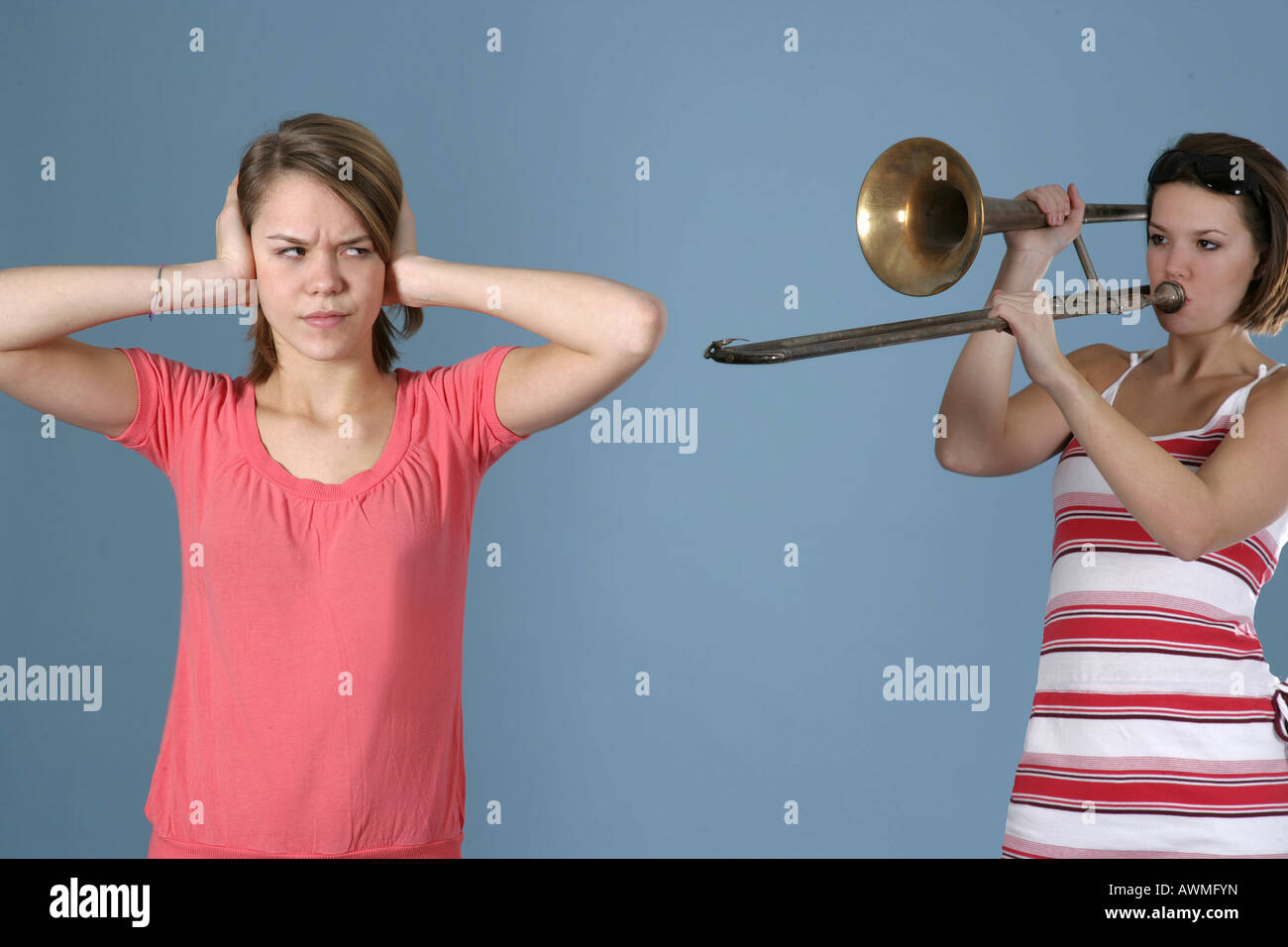 Ragazza praticare il suo trombone mentre il suo amico copre le sue orecchie, infastiditi Foto Stock