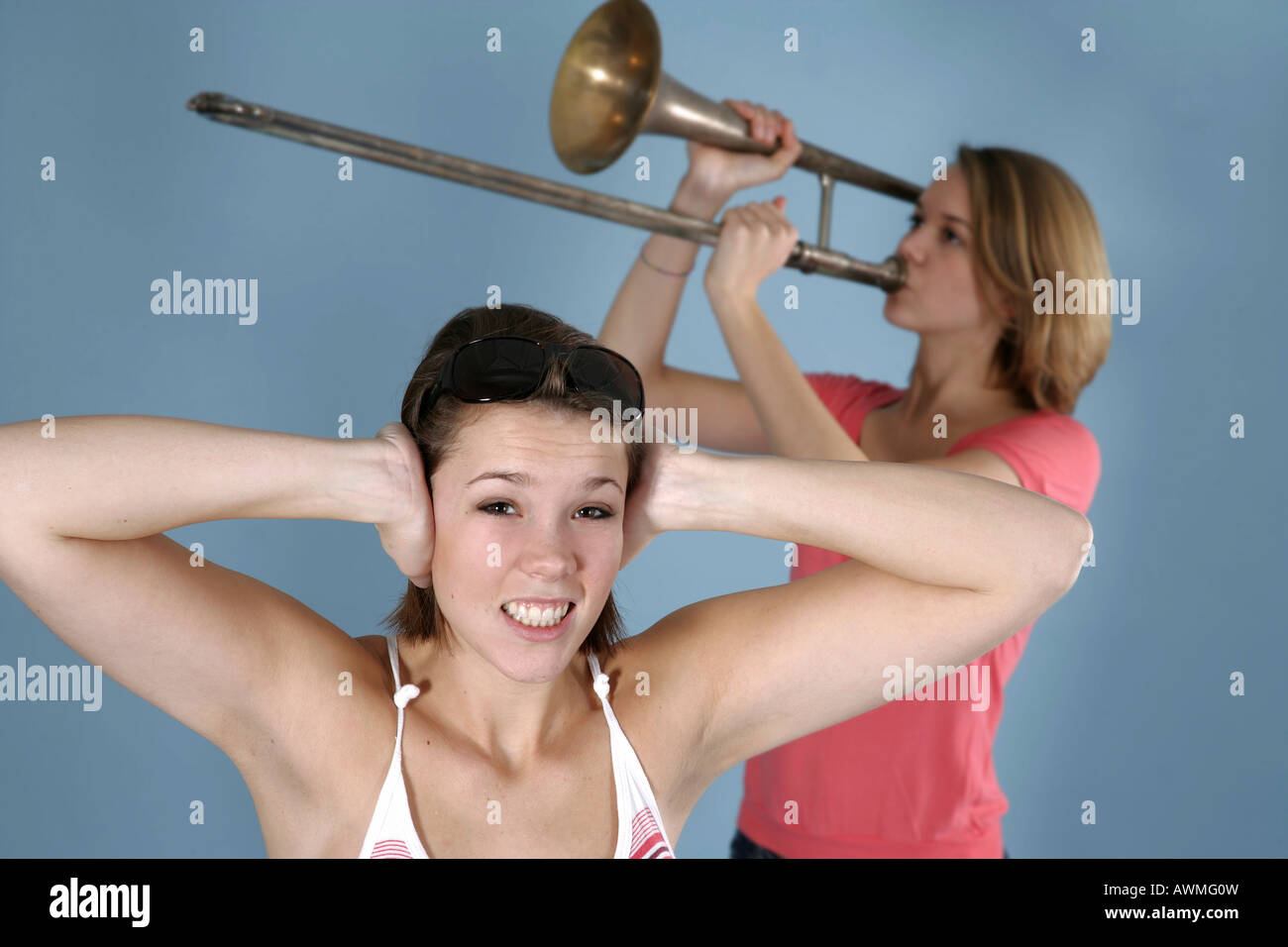 Ragazza praticare il suo trombone mentre il suo amico copre le sue orecchie, infastiditi Foto Stock