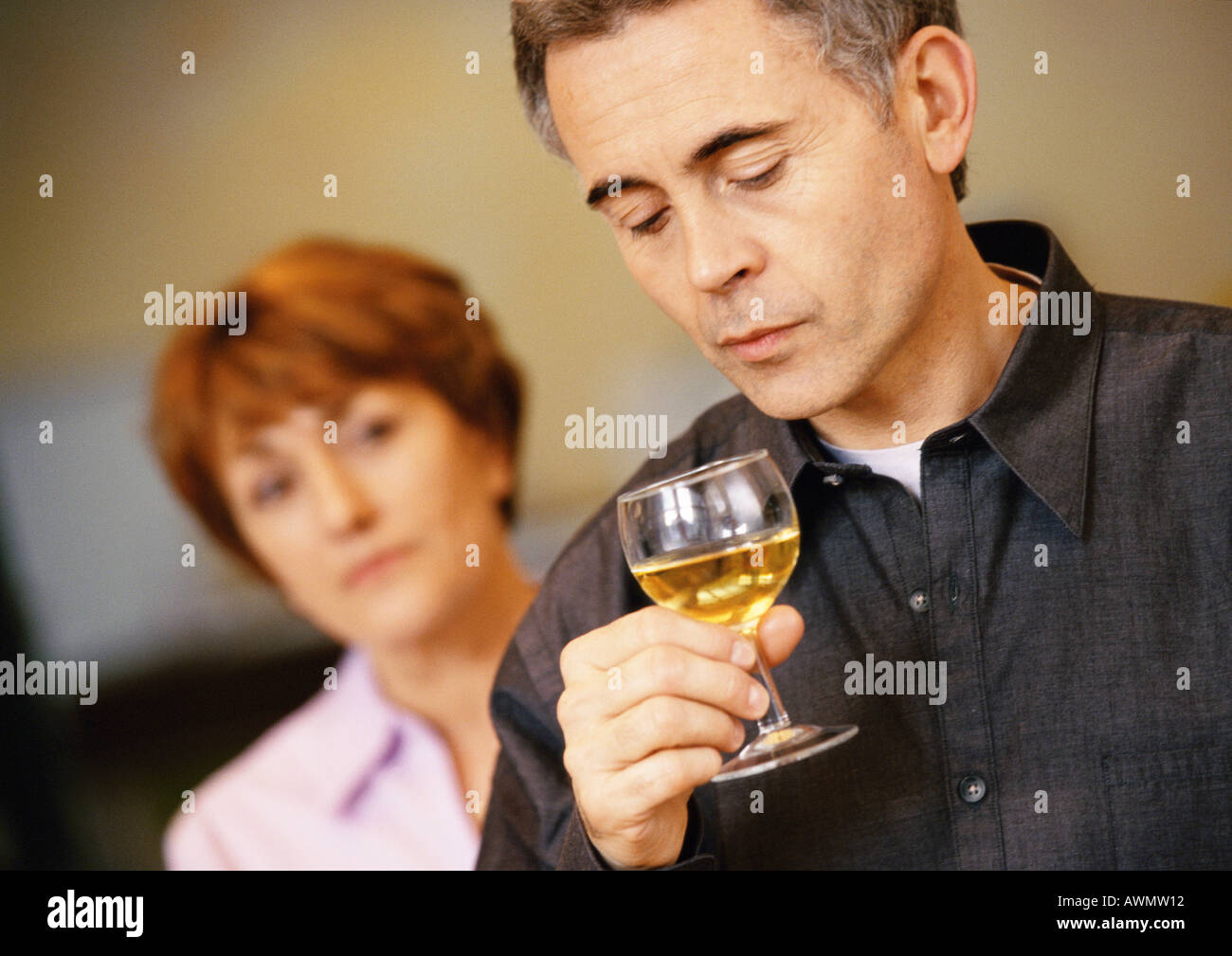 Uomo di contenimento e guardando il bicchiere da vino, donna sfocati sullo sfondo, testa e spalle, close-up Foto Stock