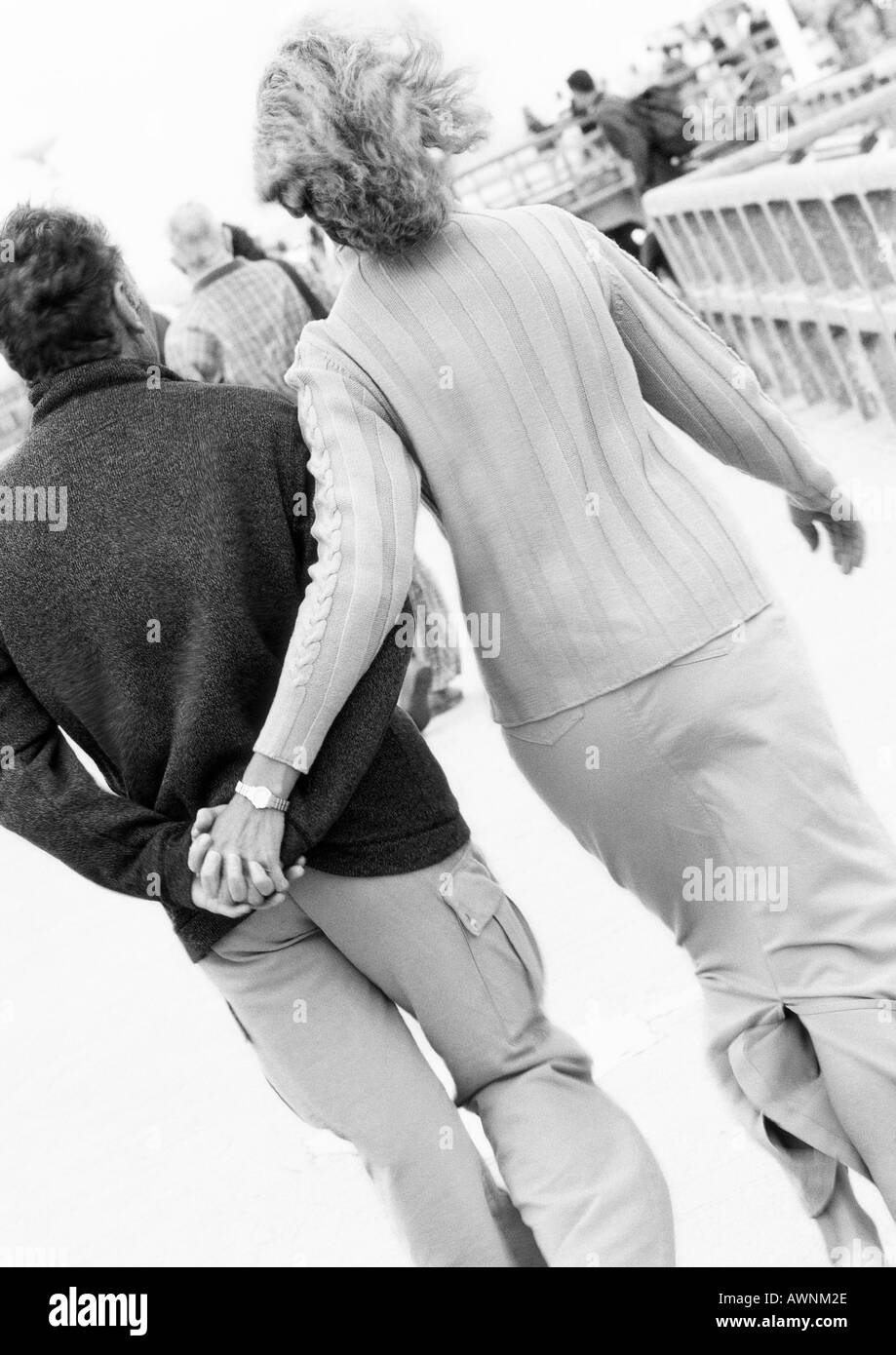 Coppia matura percorrendo a piedi il Boardwalk Holding Hands, vista posteriore, B&W Foto Stock