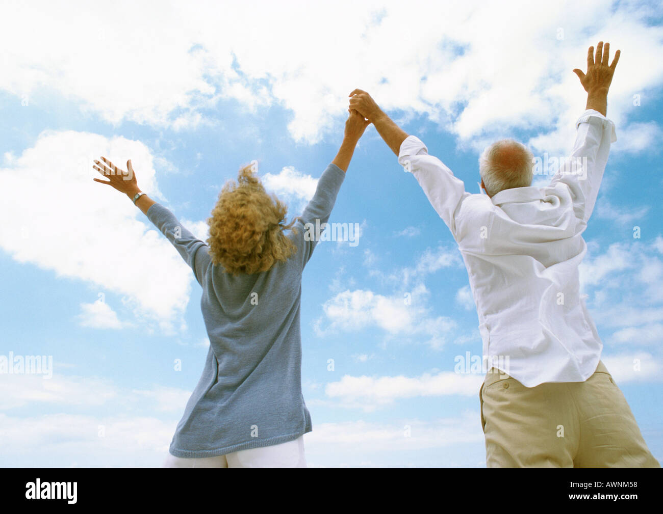 Coppia matura con le braccia in alto in aria, tenendo le mani, vista posteriore, basso angolo di visione Foto Stock