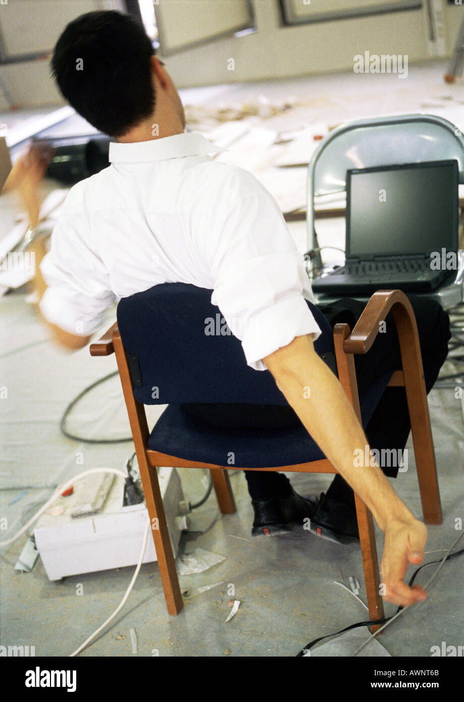 Uomo seduto in poltrona bracci di estensione, nella parte anteriore del computer portatile su una sedia Foto Stock