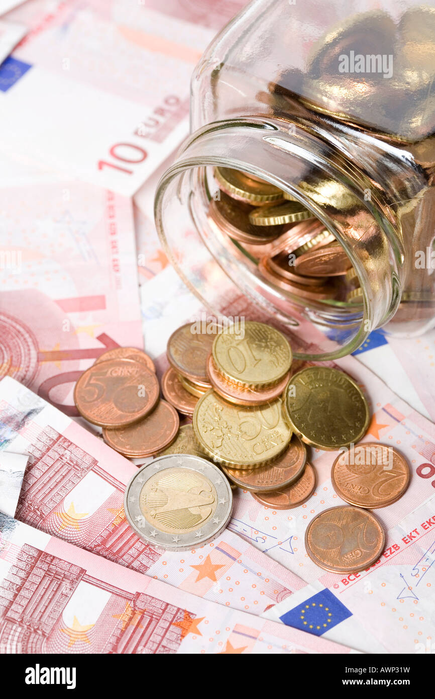 Il vasetto di vetro piena di monete sia versato su una scrivania ricoperta in contanti (Euro) Foto Stock