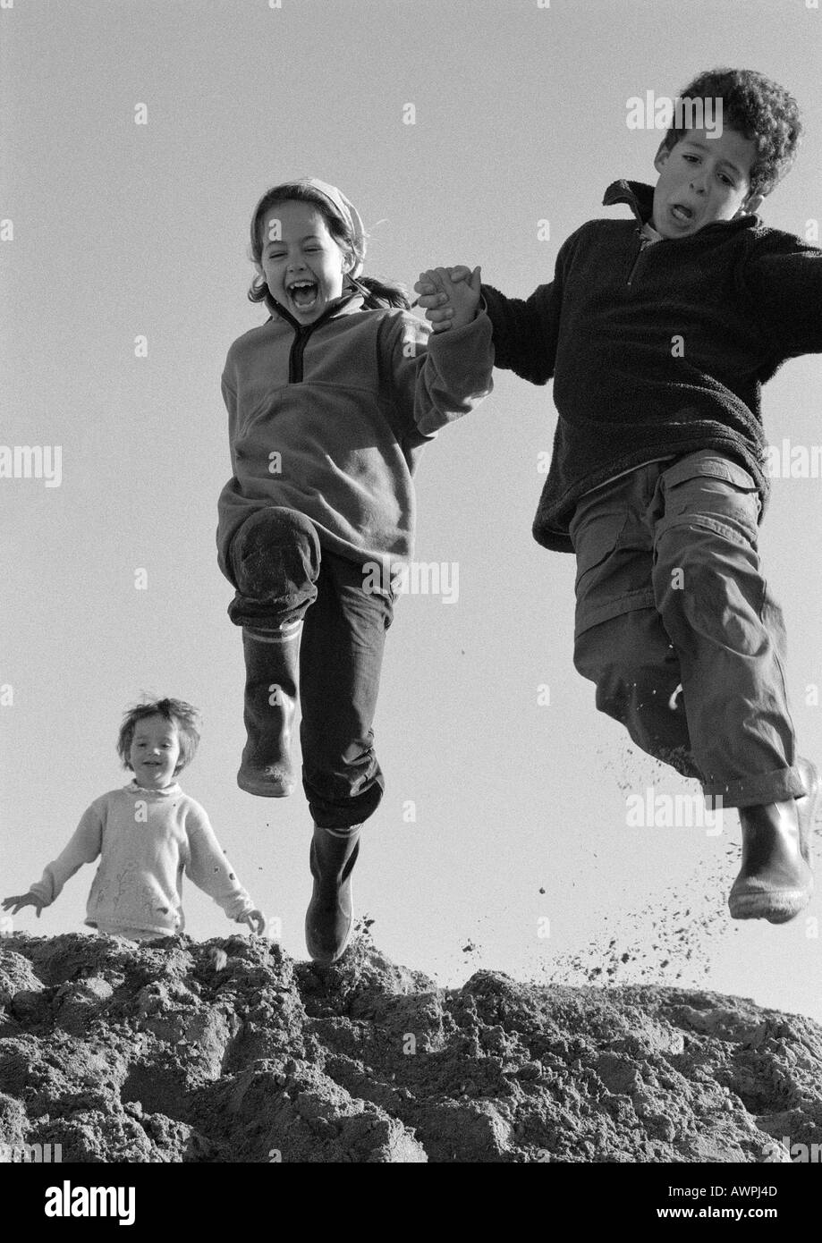 Un ragazzo e una ragazza jumping, seconda ragazza in background, a basso angolo di visione, b&W Foto Stock