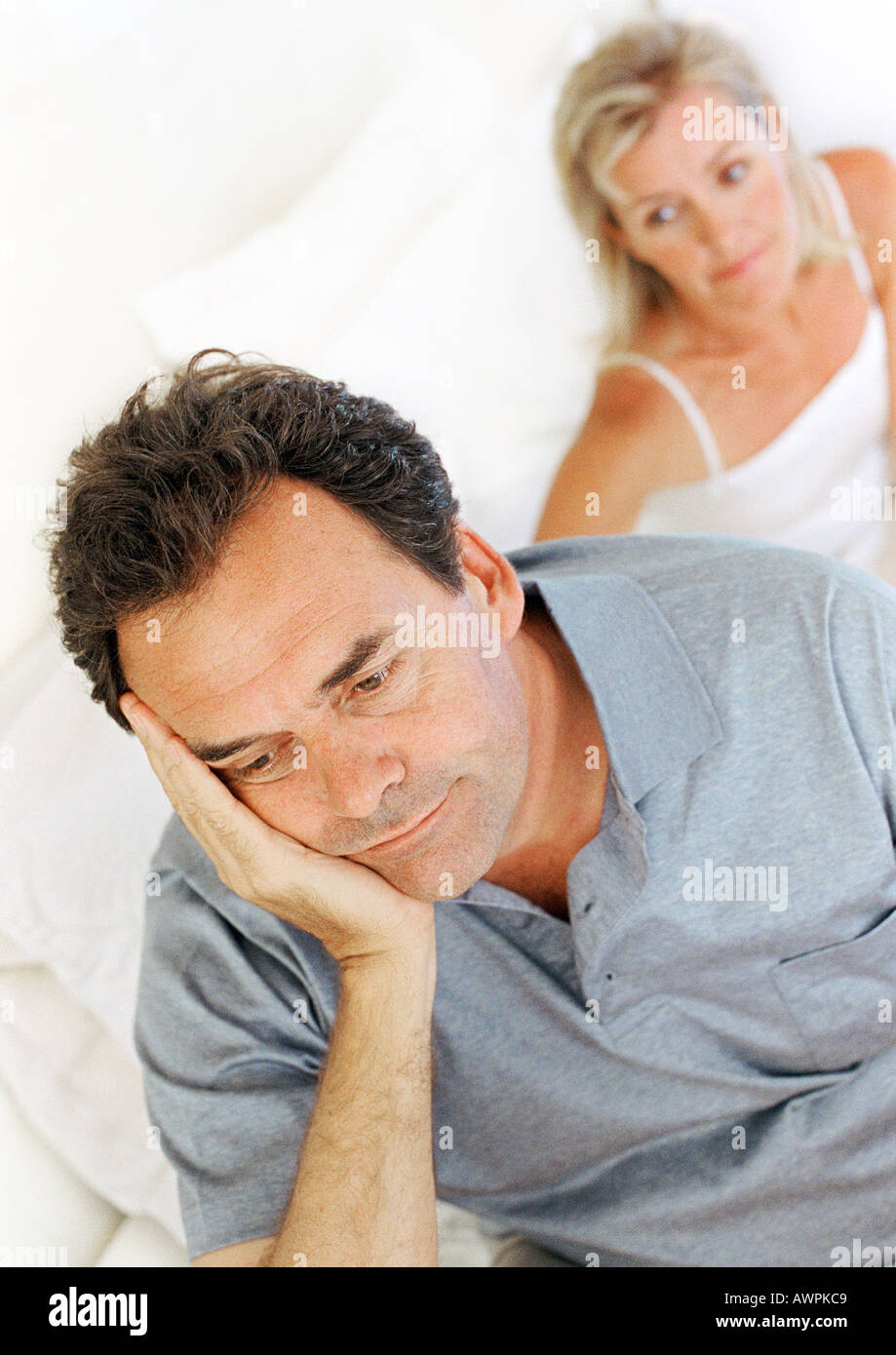 Uomo seduto sul letto, tenendo la testa, moglie in background Foto Stock