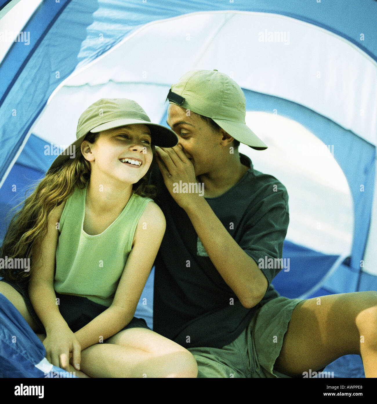Ragazzo adolescente e poco ragazza seduta tenda, ragazzo sussurra a ragazza Foto Stock