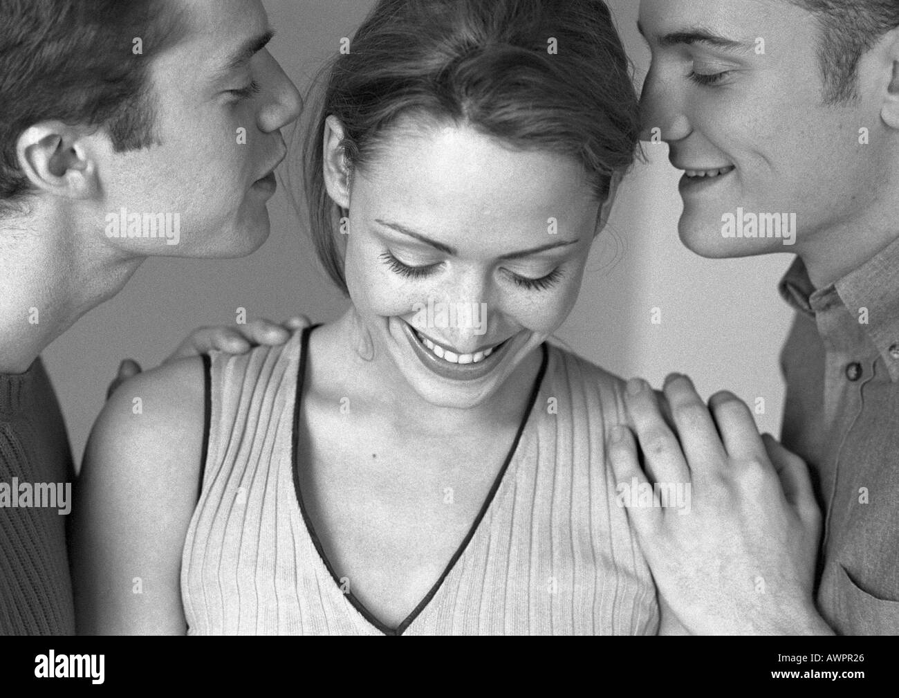 Donna in piedi tra i due uomini, sia uomini whispering per donna, close-up, b&W Foto Stock