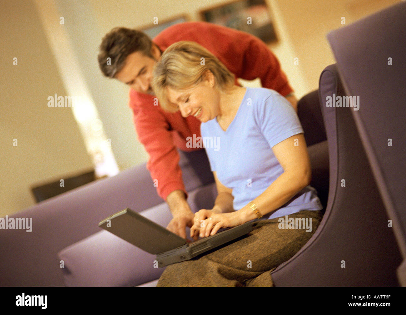 Donna matura utilizzando laptop, uomo in piedi e guardando sopra la spalla Foto Stock