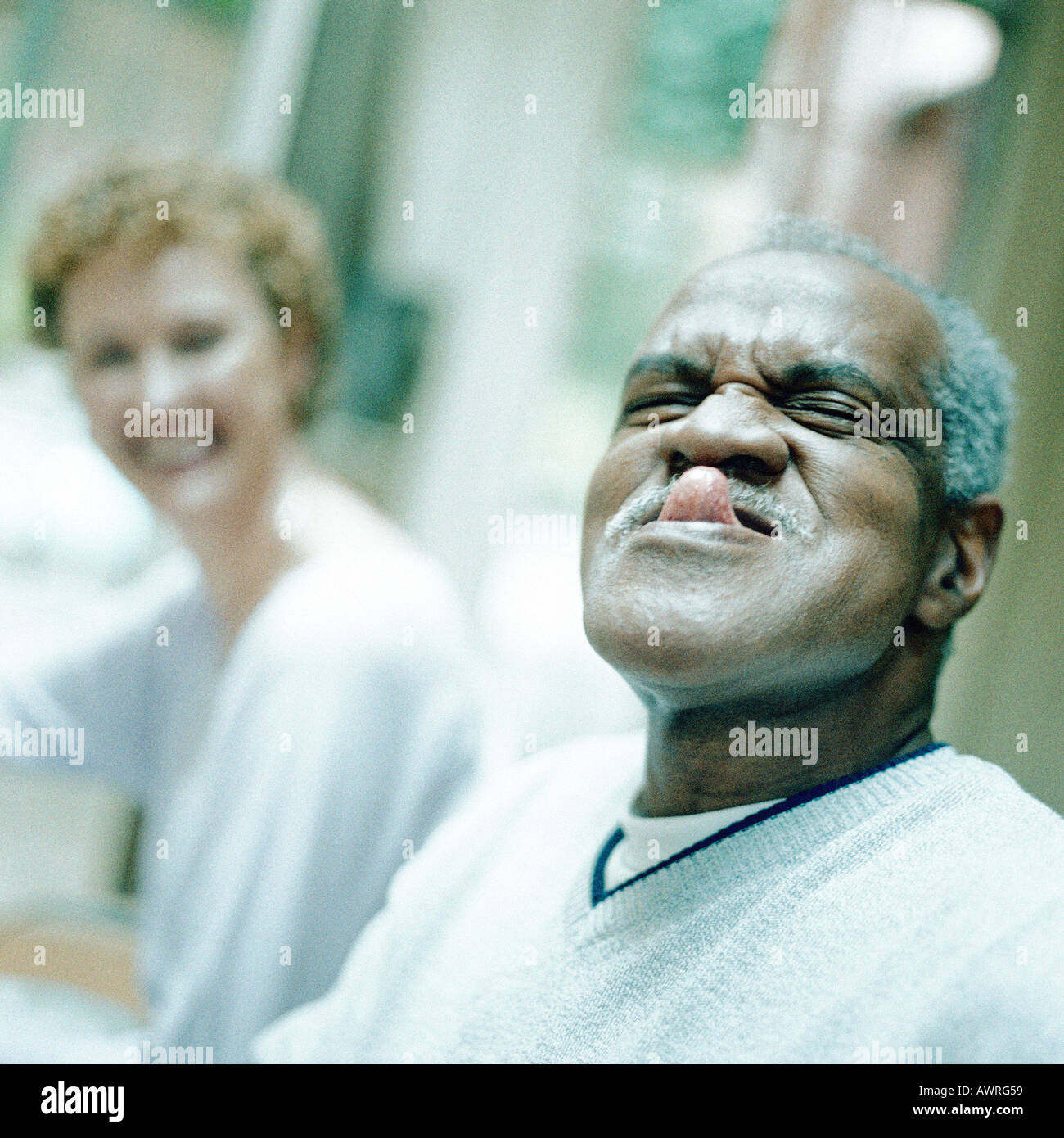 Uomo maturo spuntavano lingua, Donna sorridente in background Foto Stock