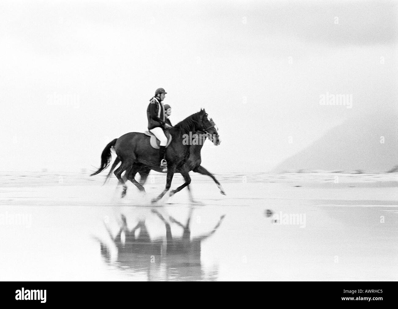 Due persone a cavallo sulla spiaggia, vista laterale, b&w. Foto Stock