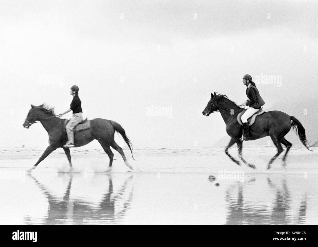 Due persone a cavallo sulla spiaggia, vista laterale, b&w. Foto Stock