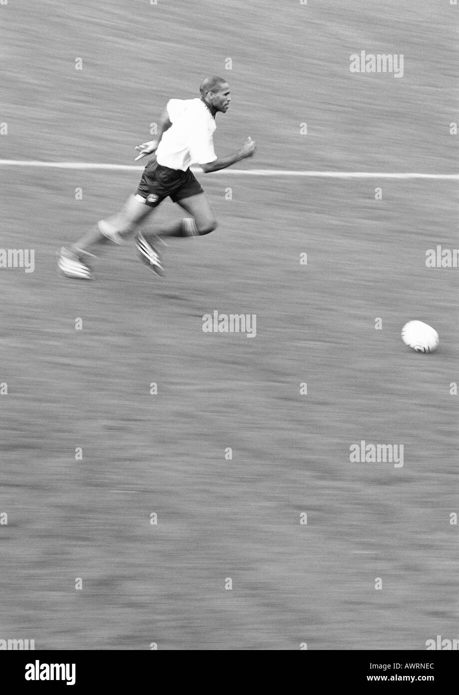 Uomo in esecuzione dopo il pallone da calcio, offuscata, b&w. Foto Stock