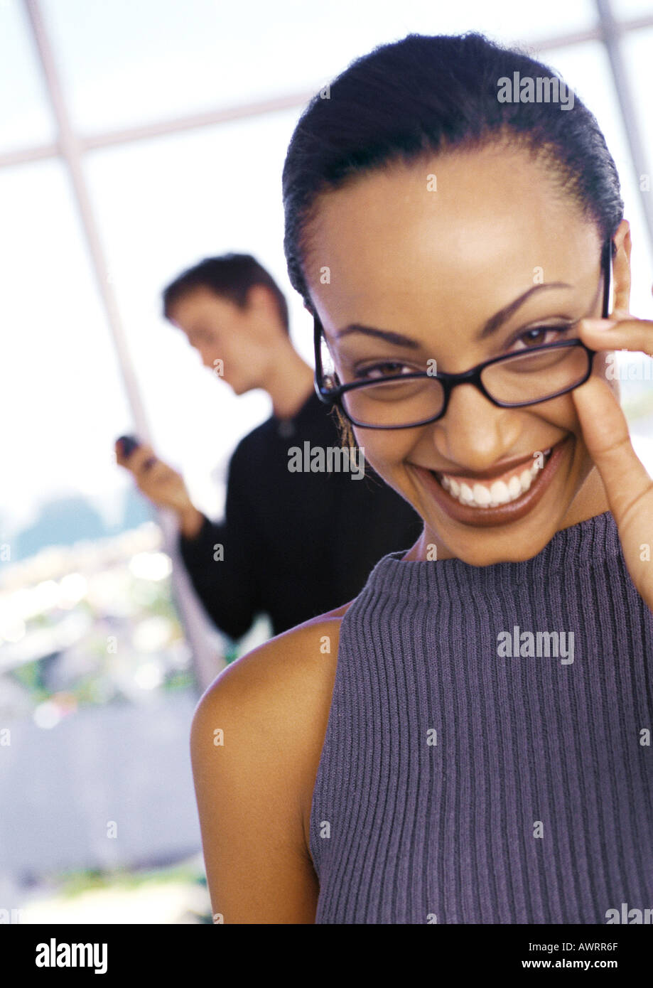 Imprenditrice Abbassamento vetri e sorridente, uomo usando il telefono in background, ritratto Foto Stock