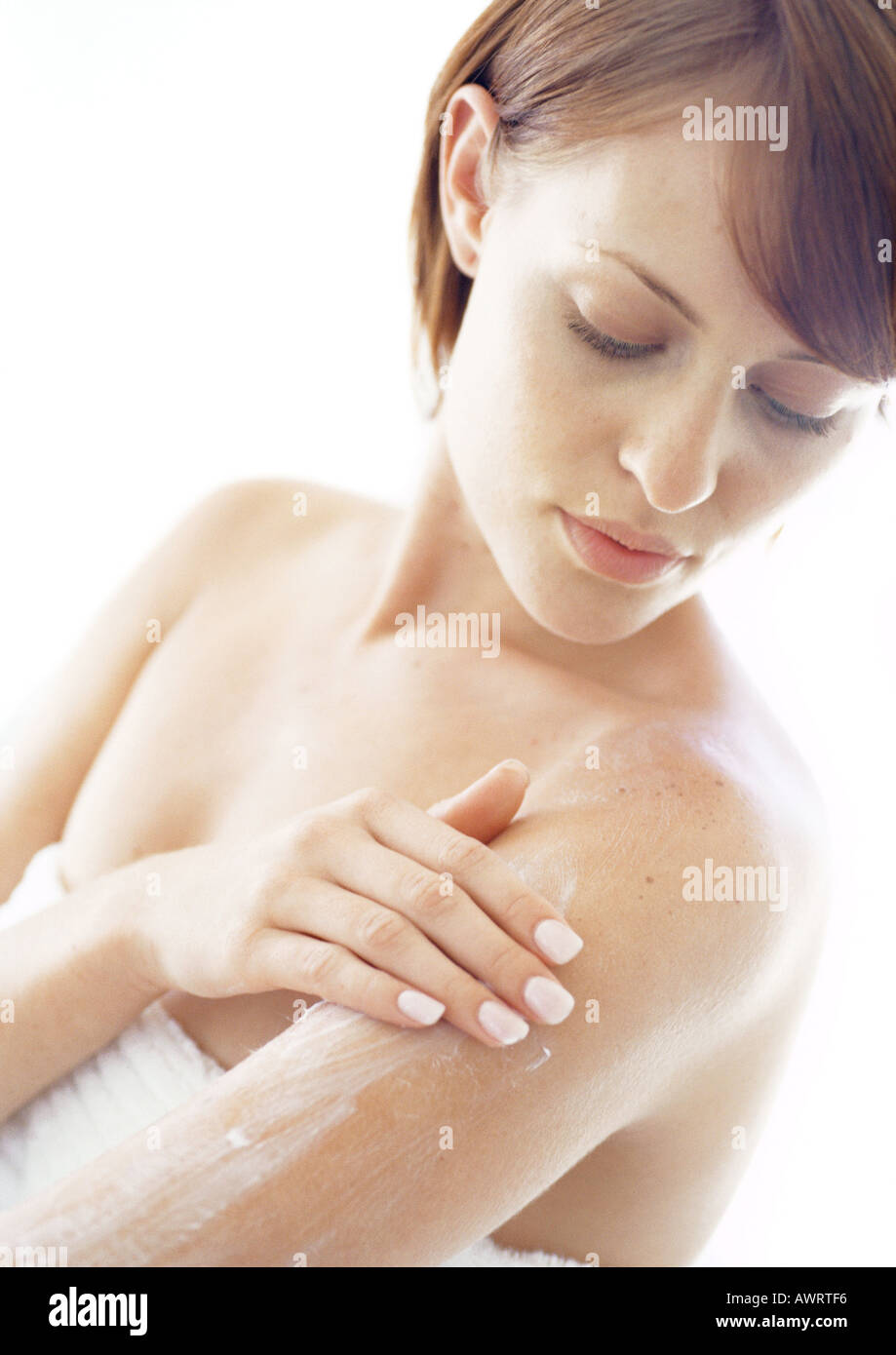 Giovane donna di applicare una crema idratante al braccio, close-up Foto Stock