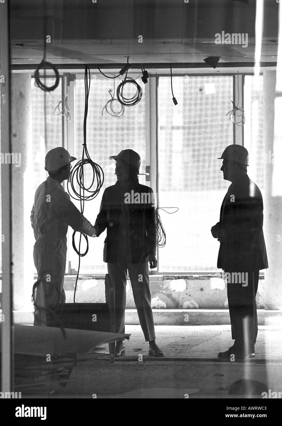 Tre persone con duro cappelli, due mani di scuotimento, b&W Foto Stock