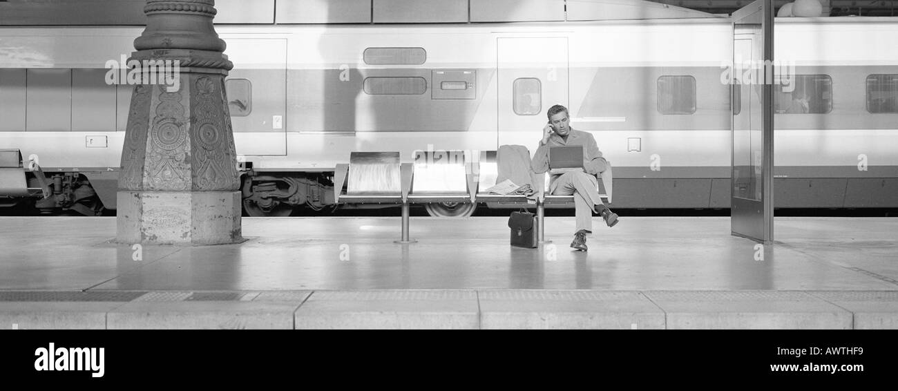 Uomo seduto al posto di guida sulla piattaforma del treno, utilizzando laptop, b&W, Vista panoramica Foto Stock