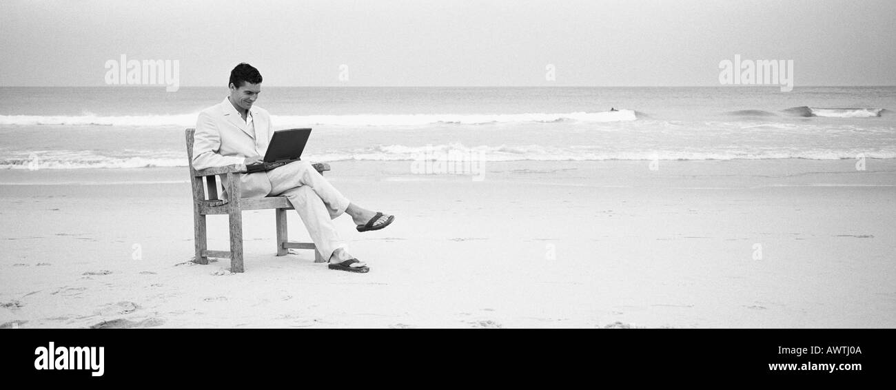 Uomo seduto nella sedia sulla spiaggia utilizzando laptop, b&W, Vista panoramica Foto Stock