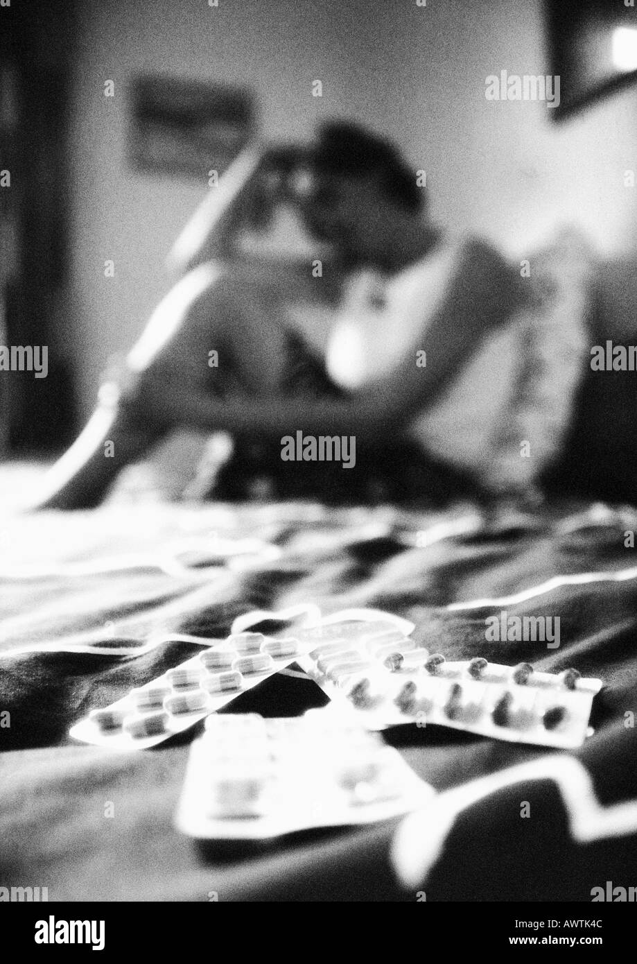 Donna seduta sul letto, pillole in primo piano sfocato, b&W Foto Stock
