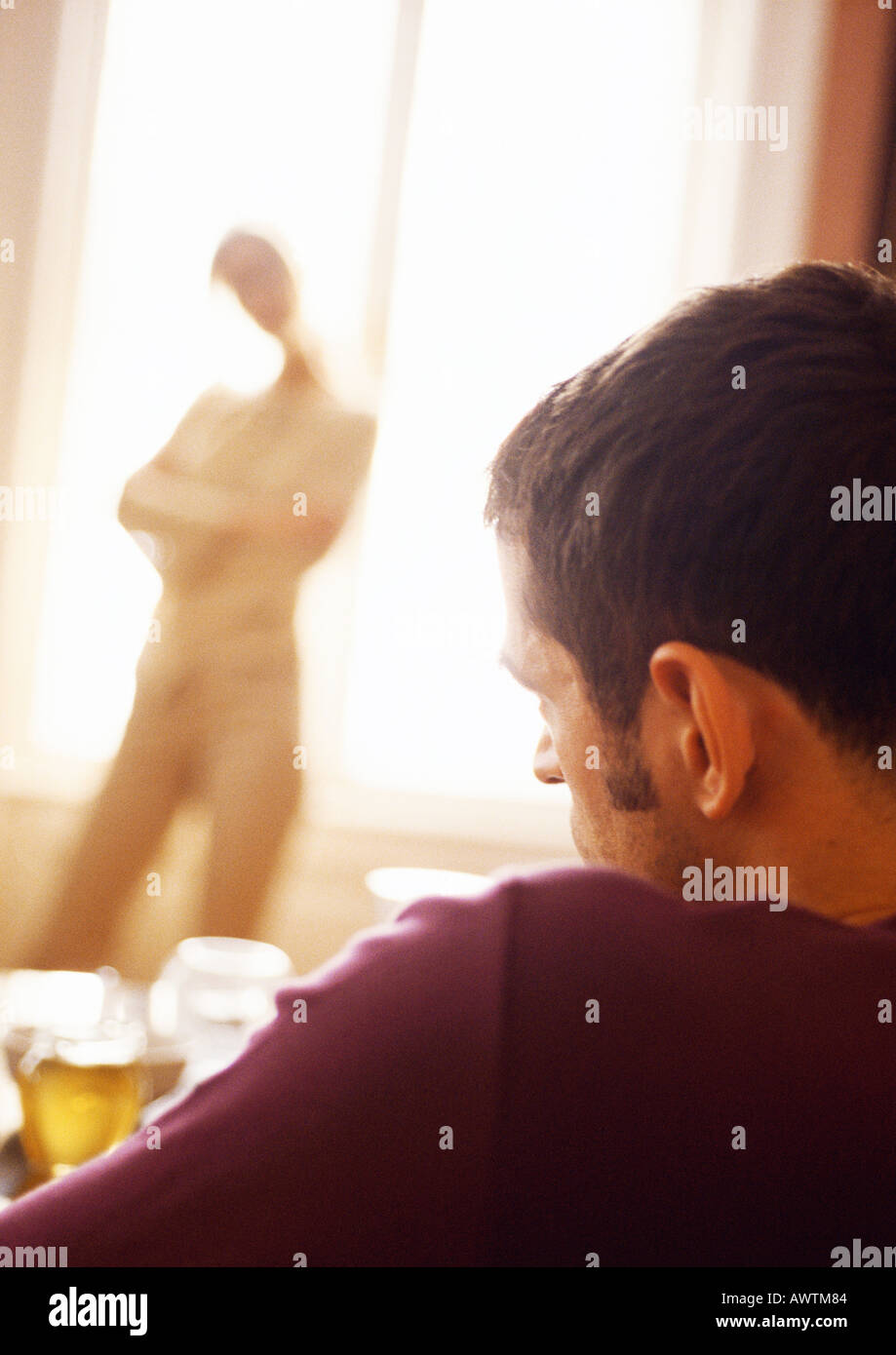 Uomo seduto, donna in piedi con le braccia incrociate davanti windown in background. Foto Stock