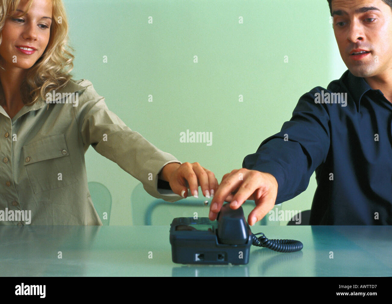 Coppia al tavolo, sia il raggiungimento di una segreteria telefonica al tempo stesso Foto Stock