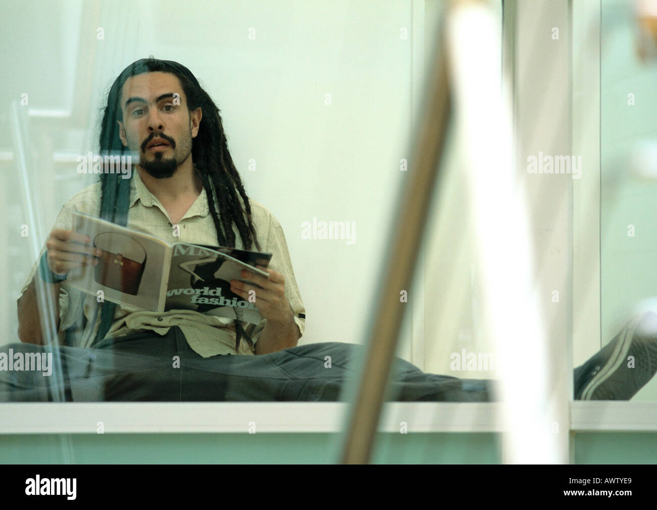 Uomo seduto a terra tenendo la rivista, cercando Foto Stock