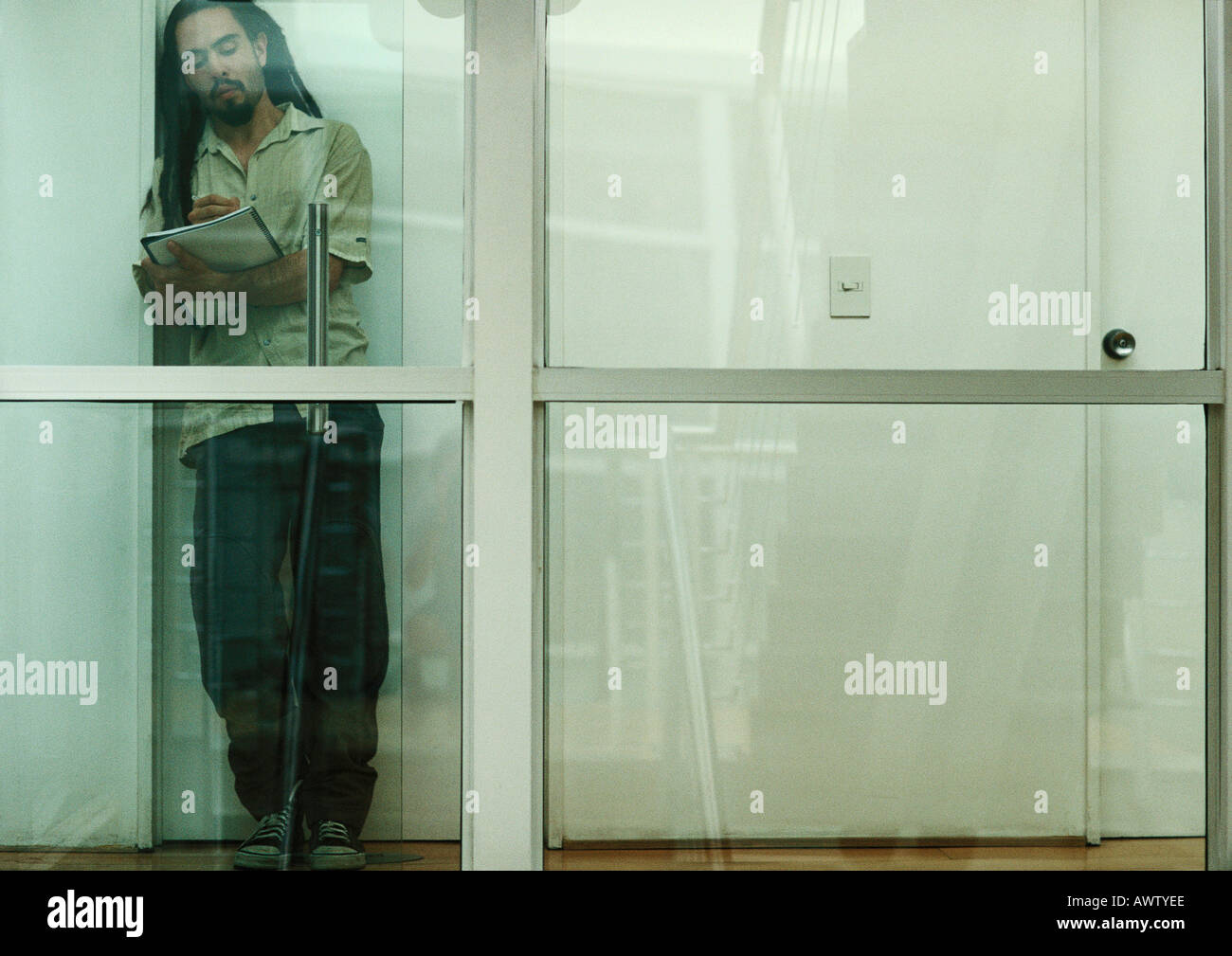 Uomo appoggiato contro la parete della lettura, vista attraverso il vetro Foto Stock