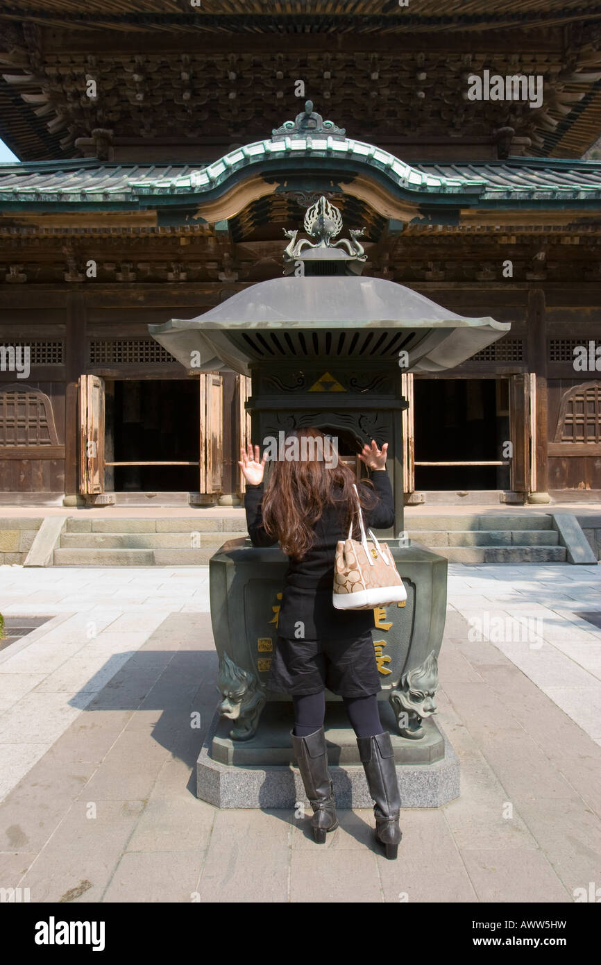 Donna sventolando il fumo su se stessa al bruciatore di incenso a Butsuden in Kenchoji Zen tempio buddista a Kamakura Giappone Foto Stock