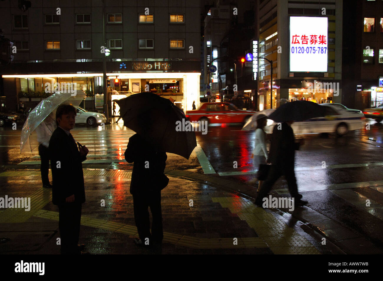 Persone con ombrelloni attraversando notte piovosa volta Tokyo street Foto Stock