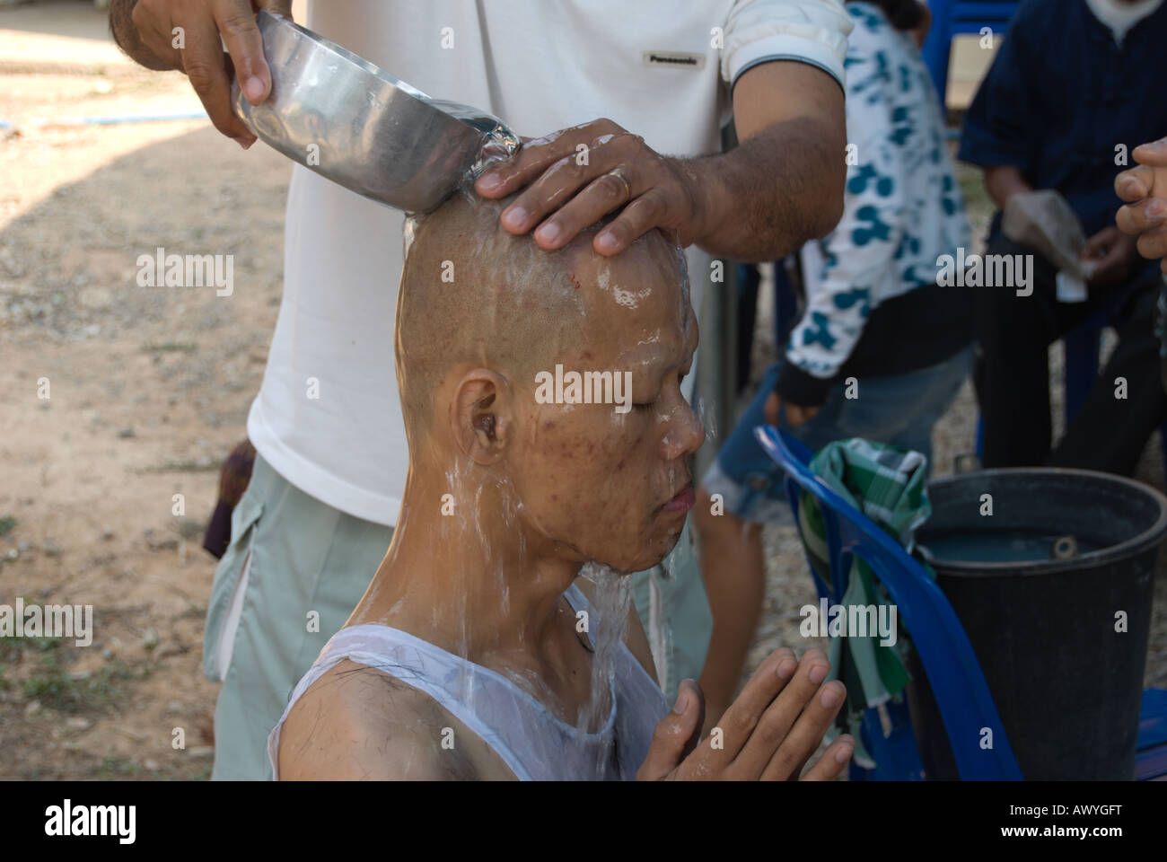 La nuova testa rasata di un monaco novizio viene lavato con acqua da parte di un membro della famiglia Foto Stock