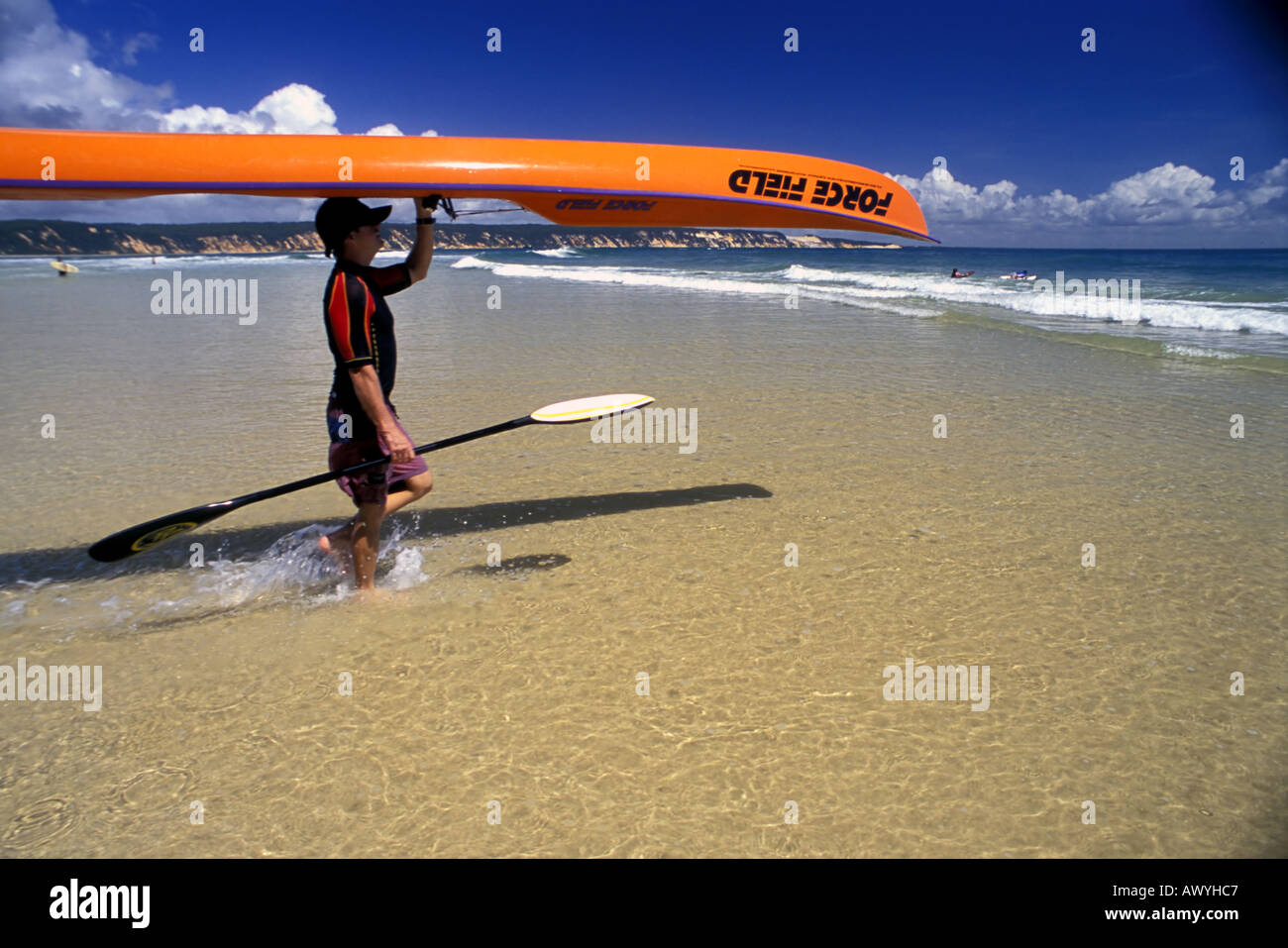 Uomo che porta surf kayak in acqua Rainbow Bay Sunshine Coast di Queensland Australia n. MR n. PR Foto Stock