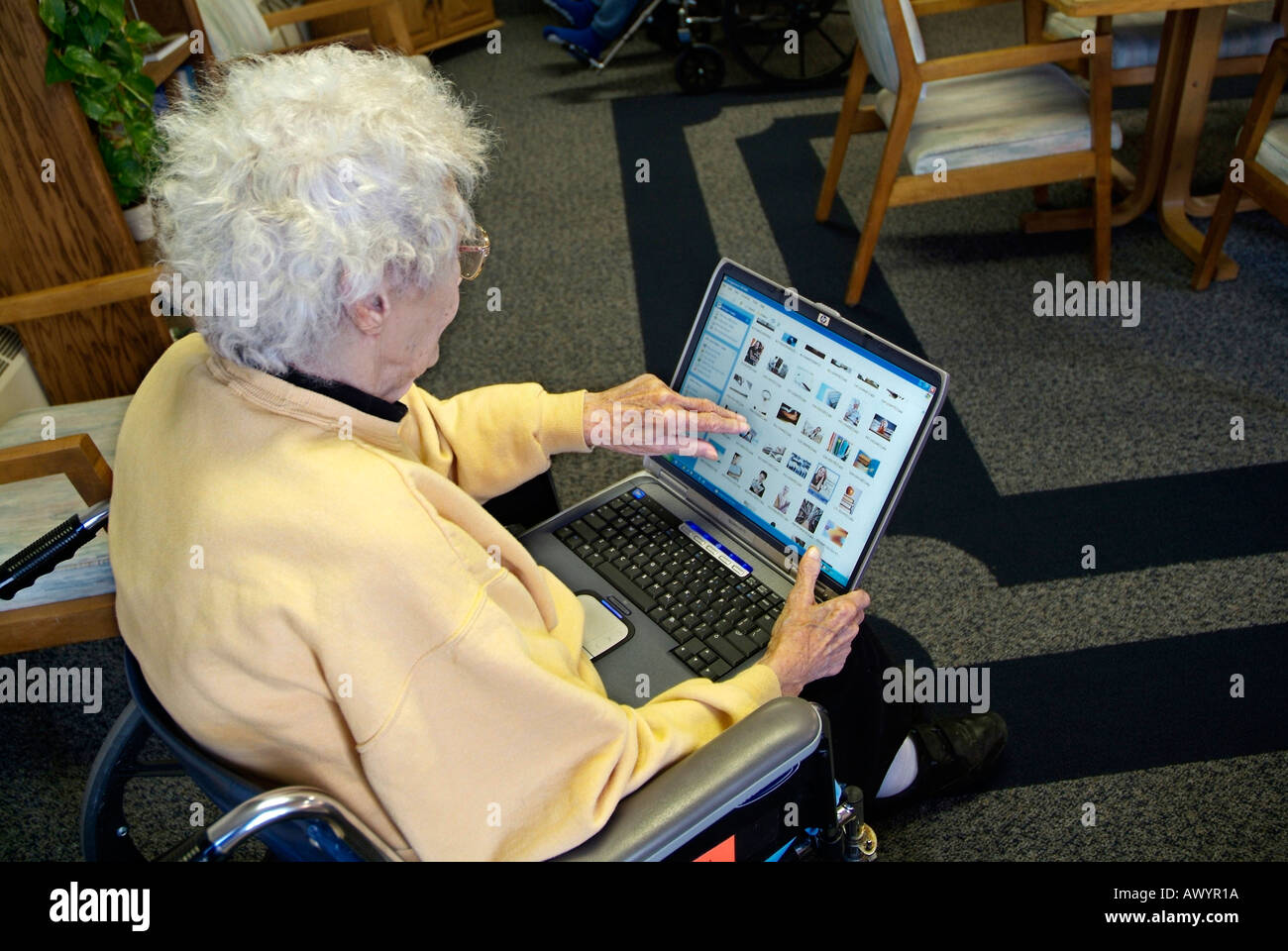 Portatori di handicap femmina Senior in una sedia a rotelle in una casa di cura controlla la posta su una connessione a internet wireless su un computer portatile Foto Stock