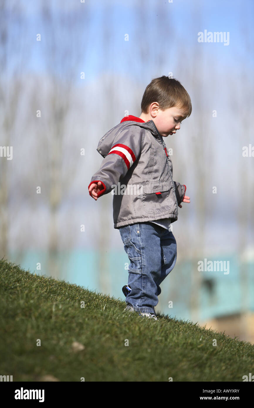 Ragazzo giovane camminando giù collina erbosa Foto Stock