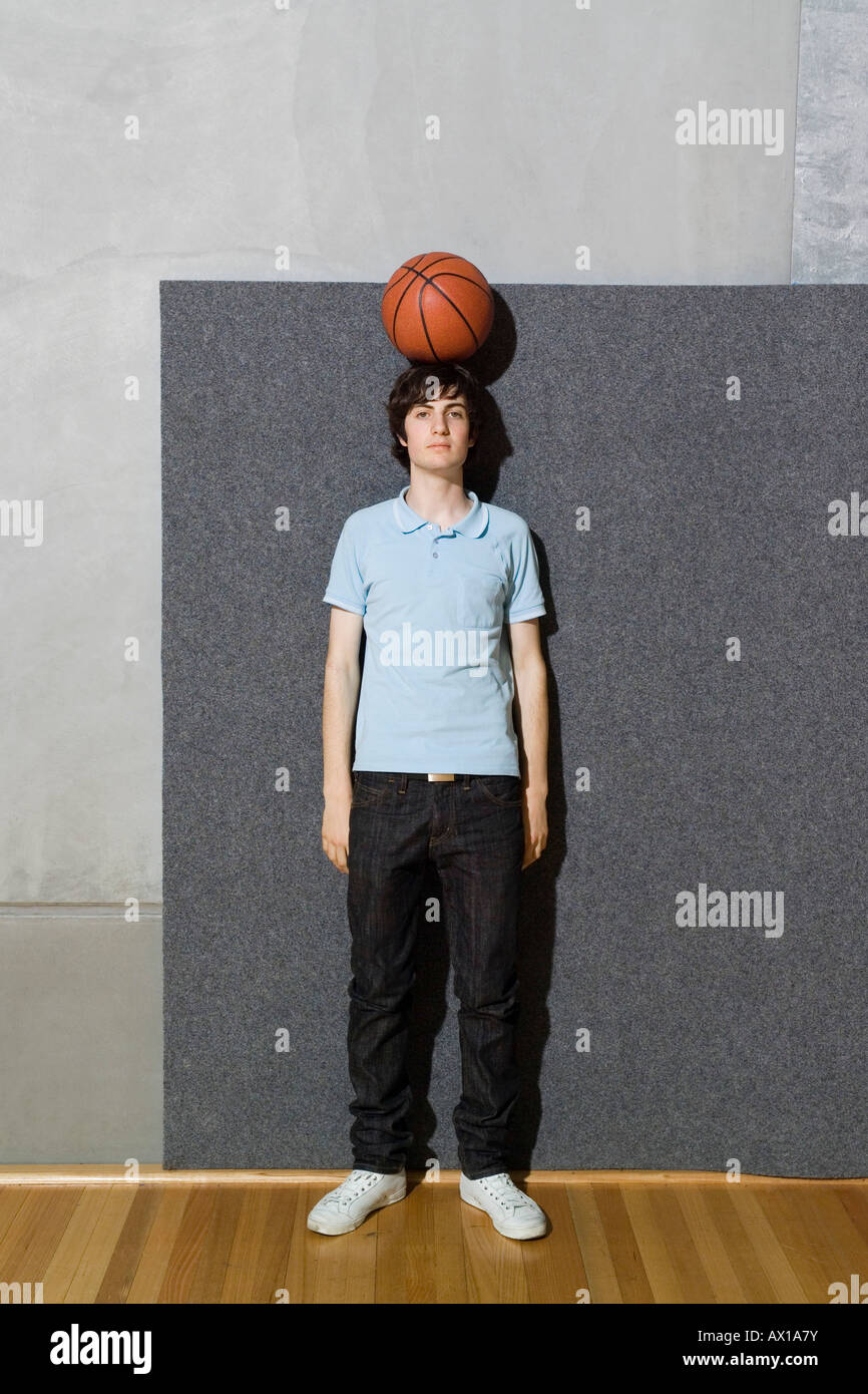 Un giovane uomo in piedi con una palla da basket bilanciato sulla sua testa Foto Stock